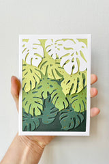 A hand holds the Monstera Laser-cut Card up for show.