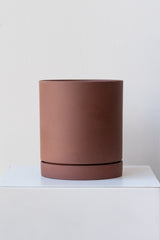 Rust medium Sekki plant pot by Ferm Living on a white pedestal in front of a white background
