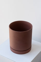 Rust medium Sekki plant pot by Ferm Living on a white pedestal in front of a white background