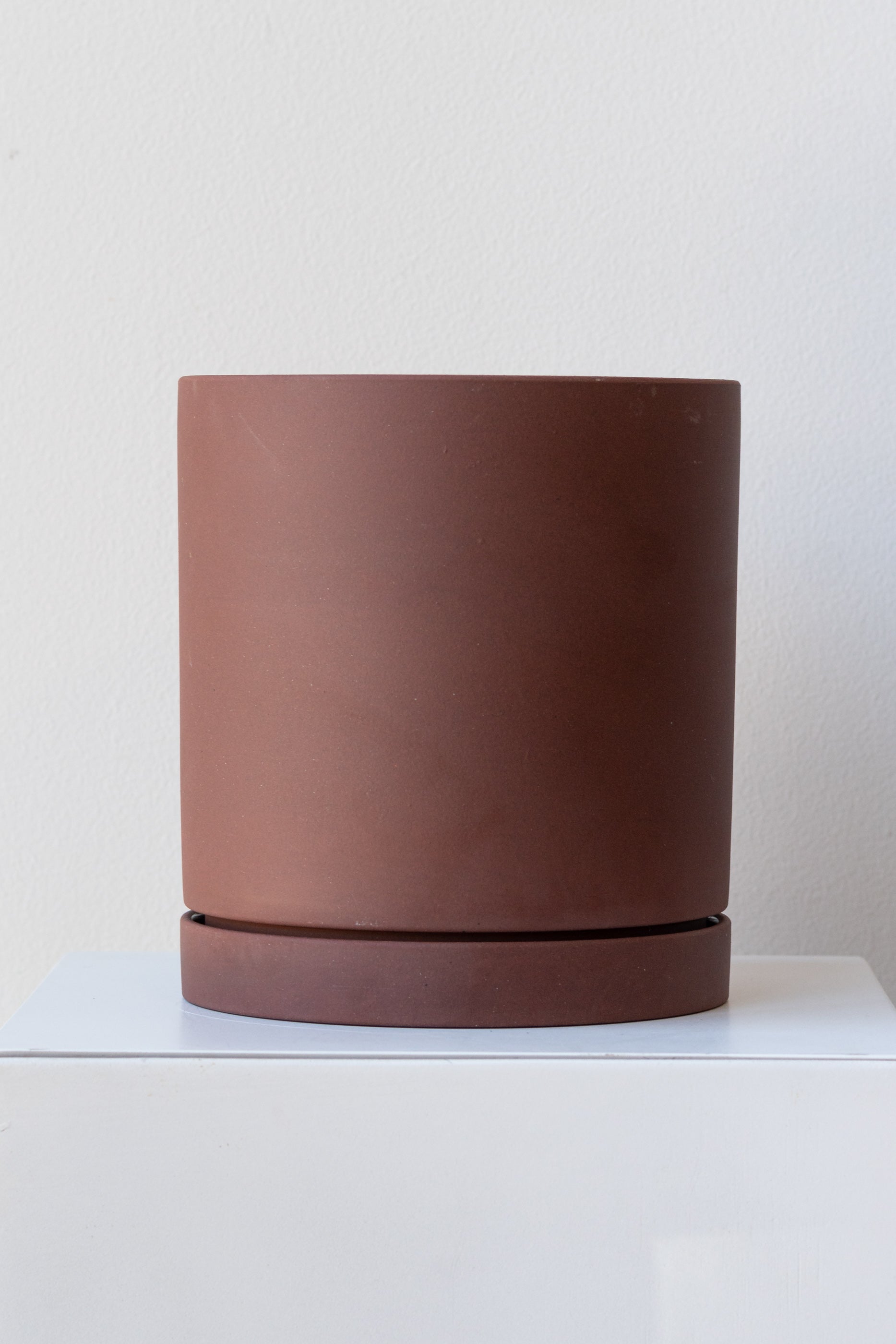 Rust large Sekki plant pot by Ferm Living on a white pedestal in front of a white background