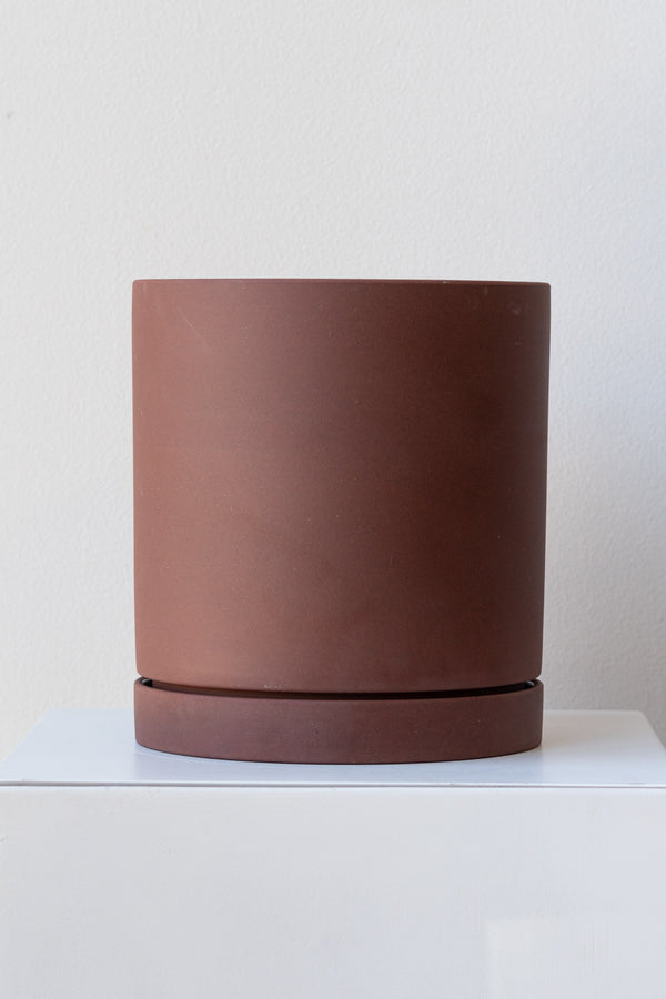Rust large Sekki plant pot by Ferm Living on a white pedestal in front of a white background