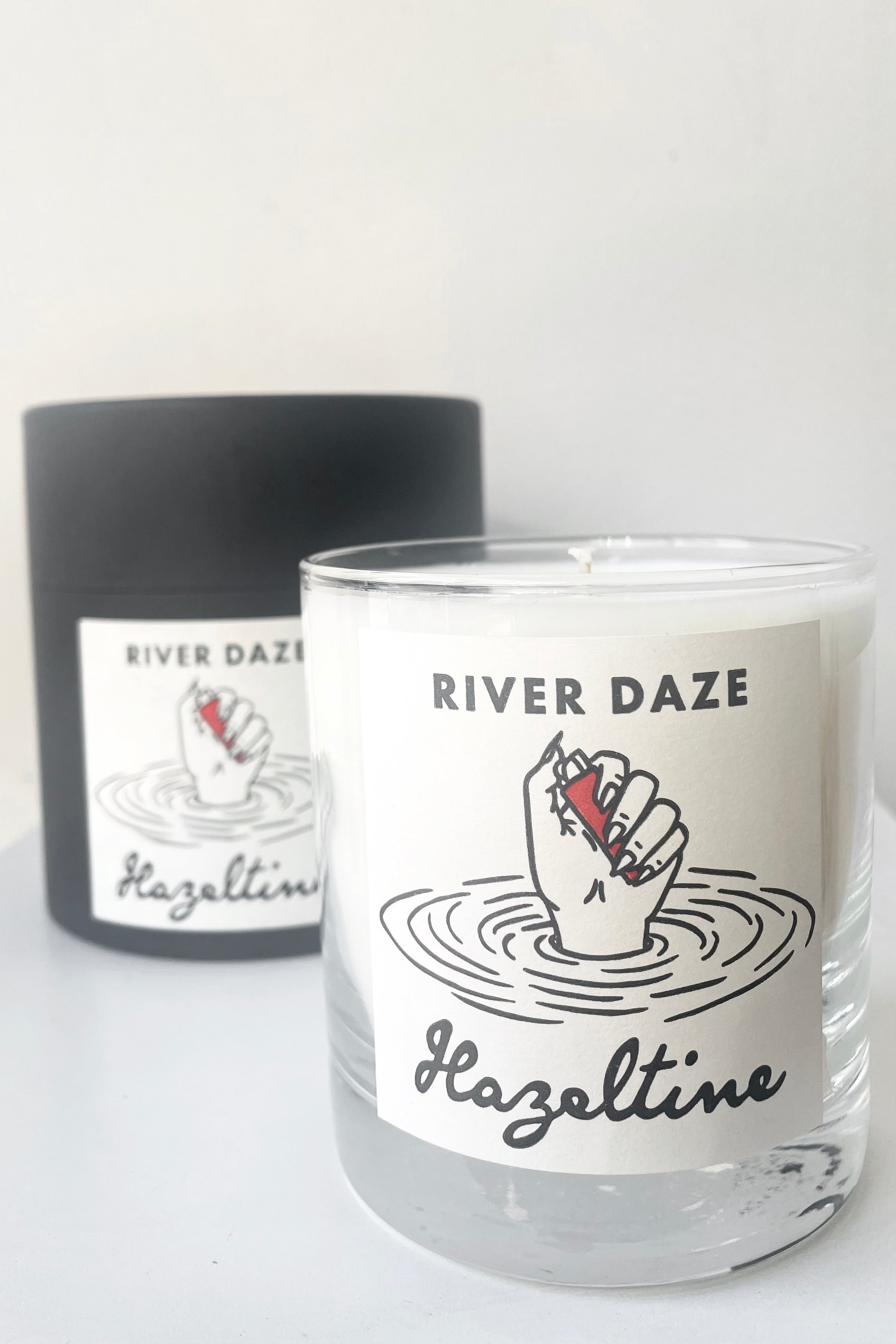 A view of packaging and candle for Hazeltine Candle river daze against white backdrop