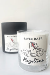 A view of packaging and candle for Hazeltine Candle river daze against white backdrop