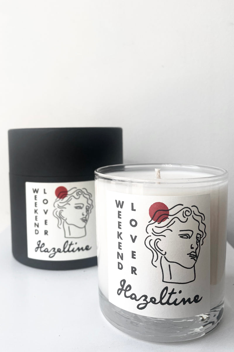 A view of packaging and candle of Hazeltine Candle weekend lover against white backdrop
