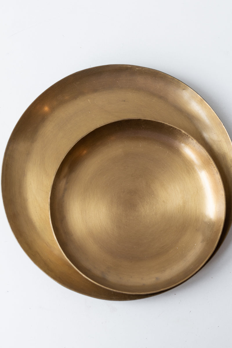 Two Fog Linen Work brass round plates, one small and one medium, on a white surface in a white room