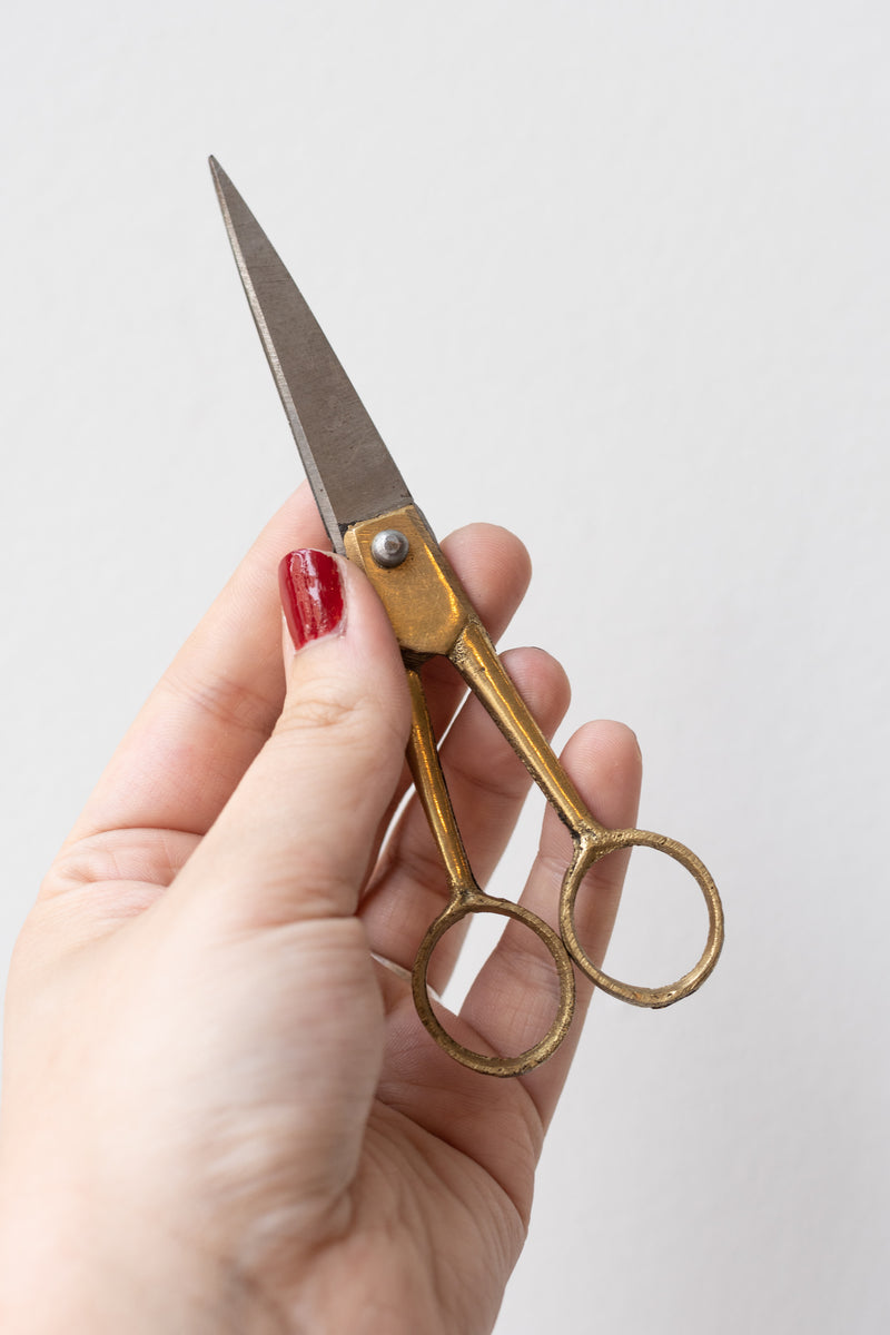 Fog Linen Work brass and steel small scissors held by a person's hand in front of a white background