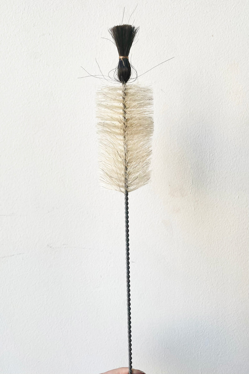 A hand holds the Small Flaschenburste Mit Kopf Bottle Brush with Head against a white backdrop