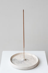 The Northern Habitat Incense Tray grey marble on a white surface in a white room. Inside the holder is a single stick of incense