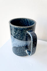Mug blue aoirabo detail of ceramic mug with dark and light blue glaze against a white platform and wall