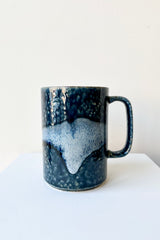 Mug blue aoirabo ceramic mug with dark and light blue glaze against a white platform and wall