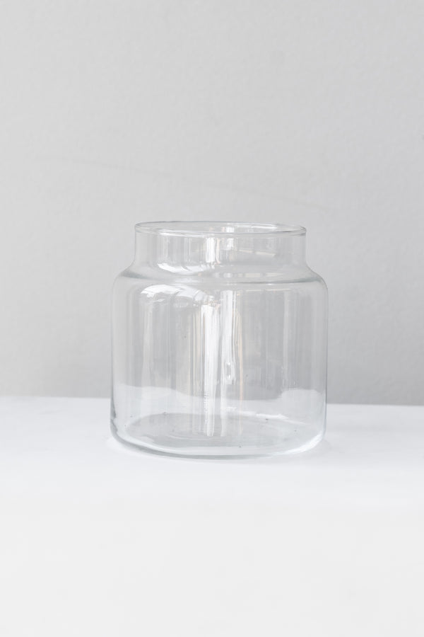 Clear glass jar sits on a white surface in a white room. It is photographed straight on.