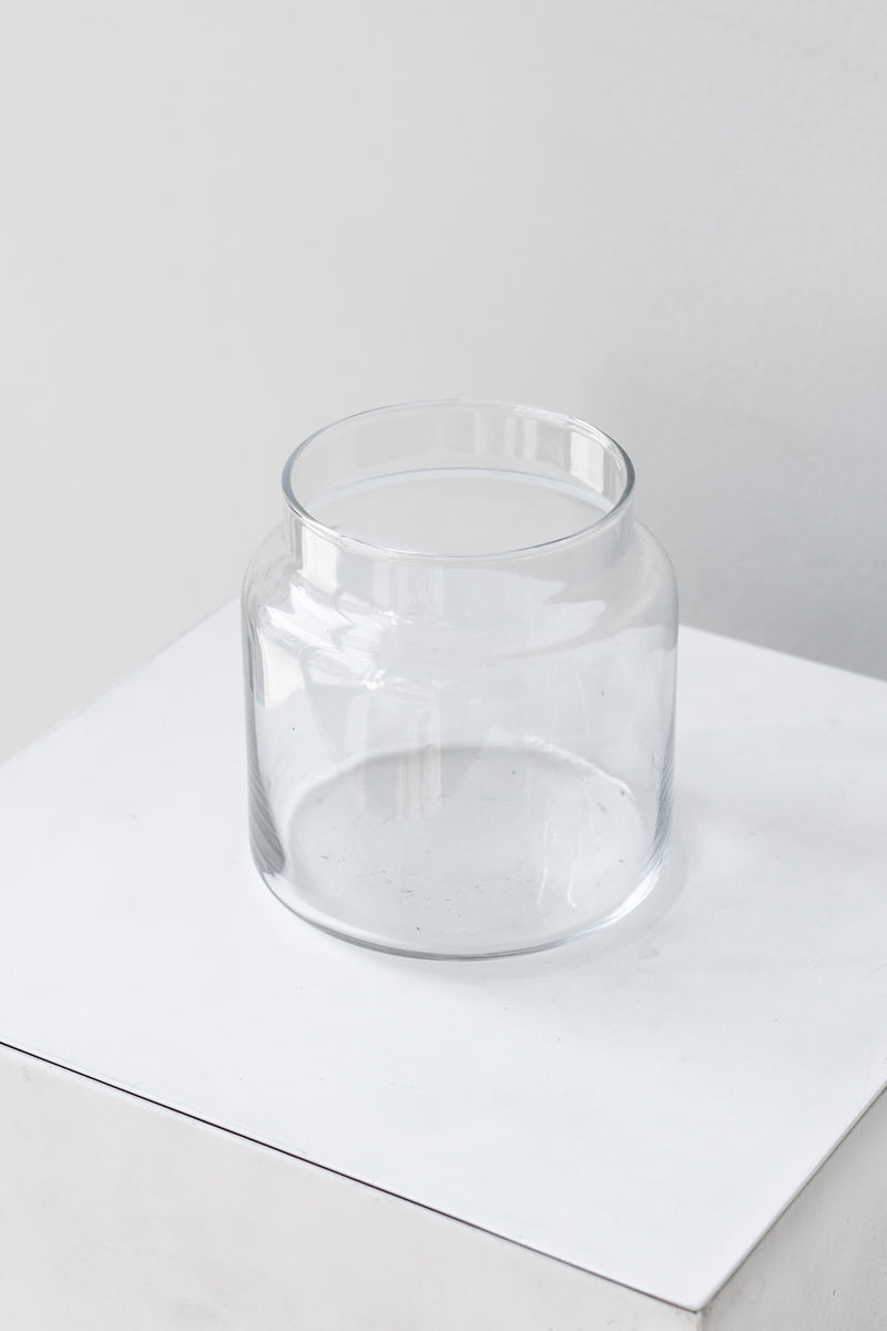 Clear glass jar sits on a white surface in a white room. It is photographed closer and at an angle.