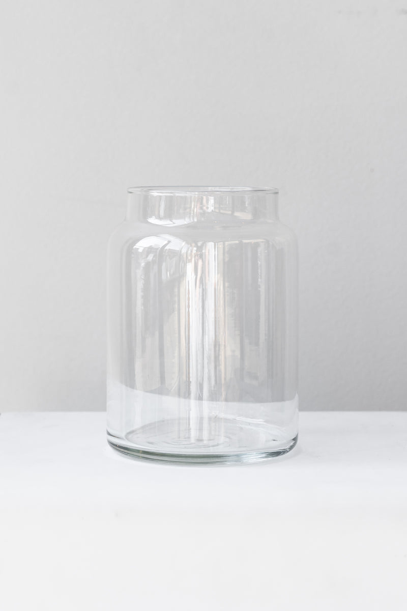 Clear glass jar sits on a white surface in a white room. It is photographed straight on.