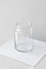 Clear glass jar sits on a white surface in a white room. It is photographed closer and at an angle.