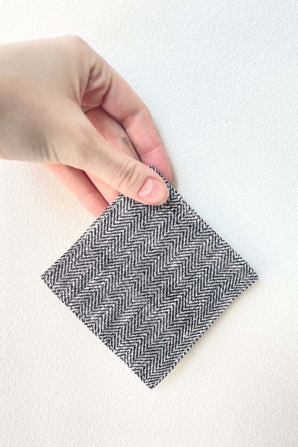 Black Herringbone Linen Coaster held against a white wall