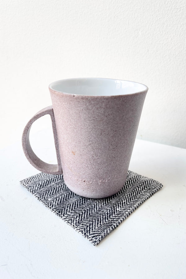 Black Herringbone Linen Coaster under a purple mug against a white wall