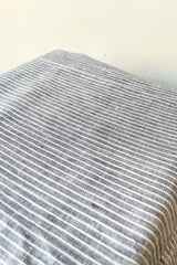 A detailed view of the grey with white stripe linen tablecloth against a white background