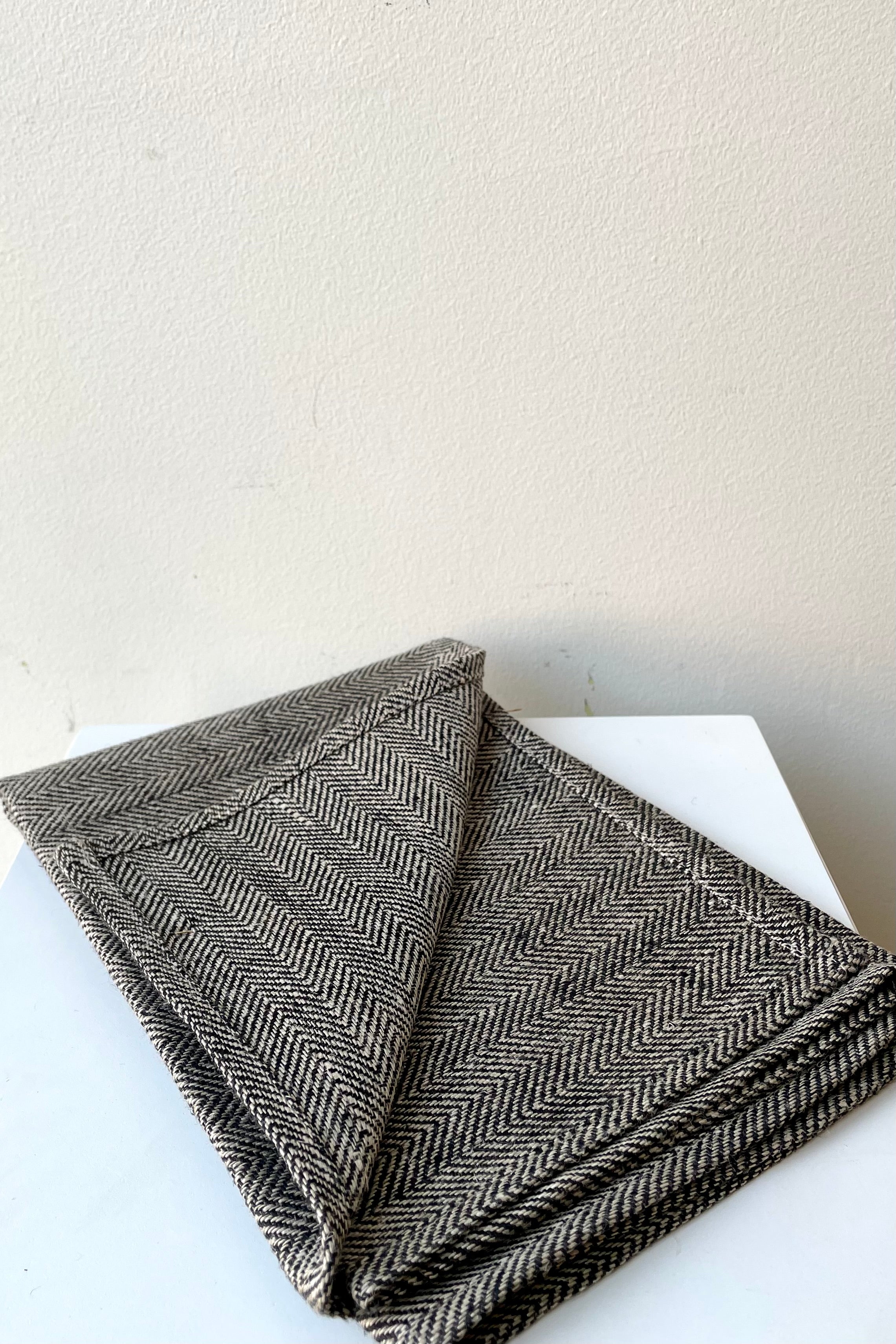 A slight overhead view of the Kitchen Cloth linen black herringbone napkin against a white background