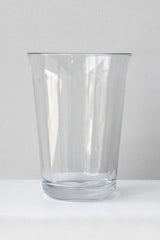 Clear fluted glass vase sits on a white surface in a white room. It is photographed straight on.