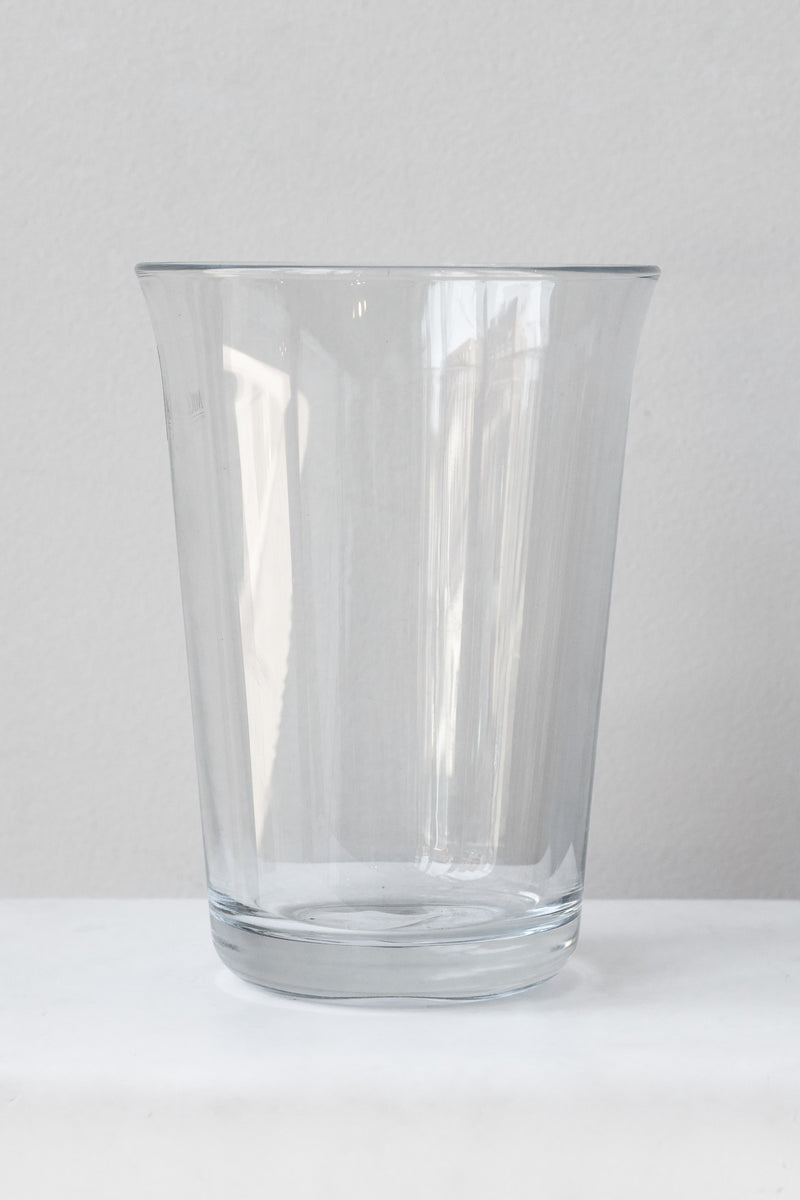 Clear fluted glass vase sits on a white surface in a white room. It is photographed straight on.