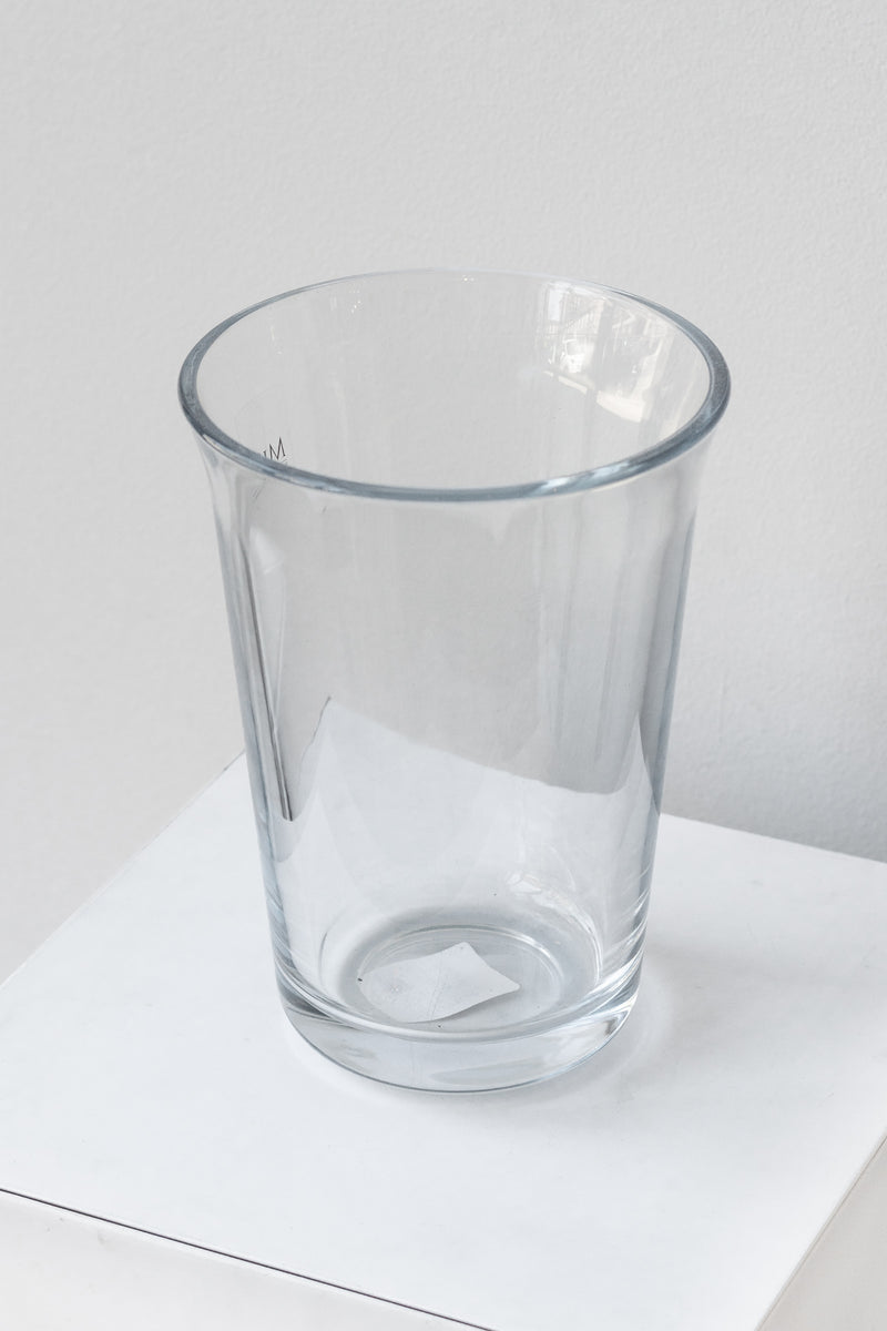 Clear fluted glass vase sits on a white surface in a white room. It is photographed closer and at an angle. 