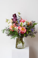 Large Dawn floral arrangement by Sprout Home sits in a clear vase on a white pedestal in a white room
