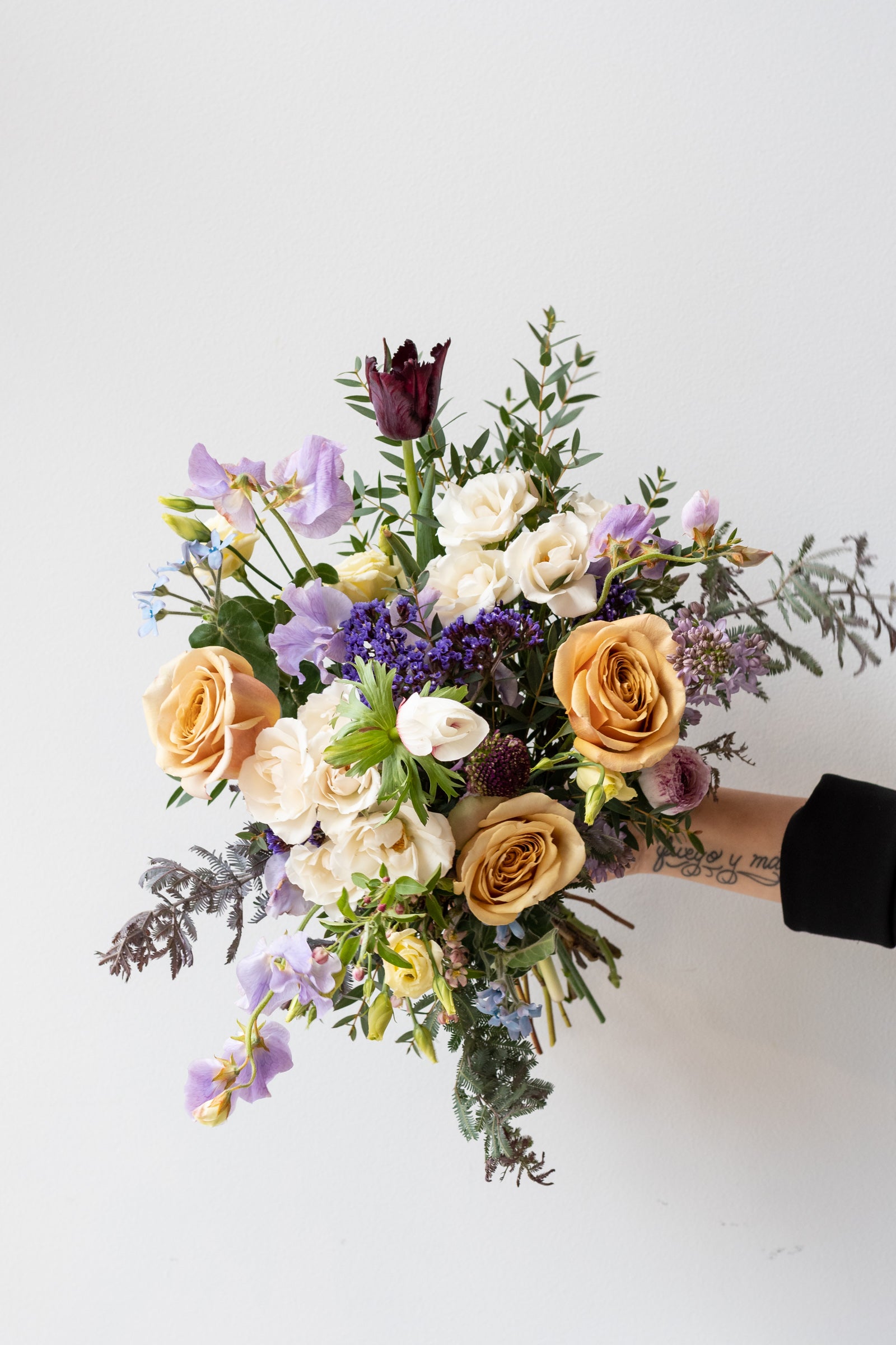 Hand holding Dawn floral arrangement by Sprout home with purple sweet pea and golden roses in front of white background ©Sprout Home #size_$130