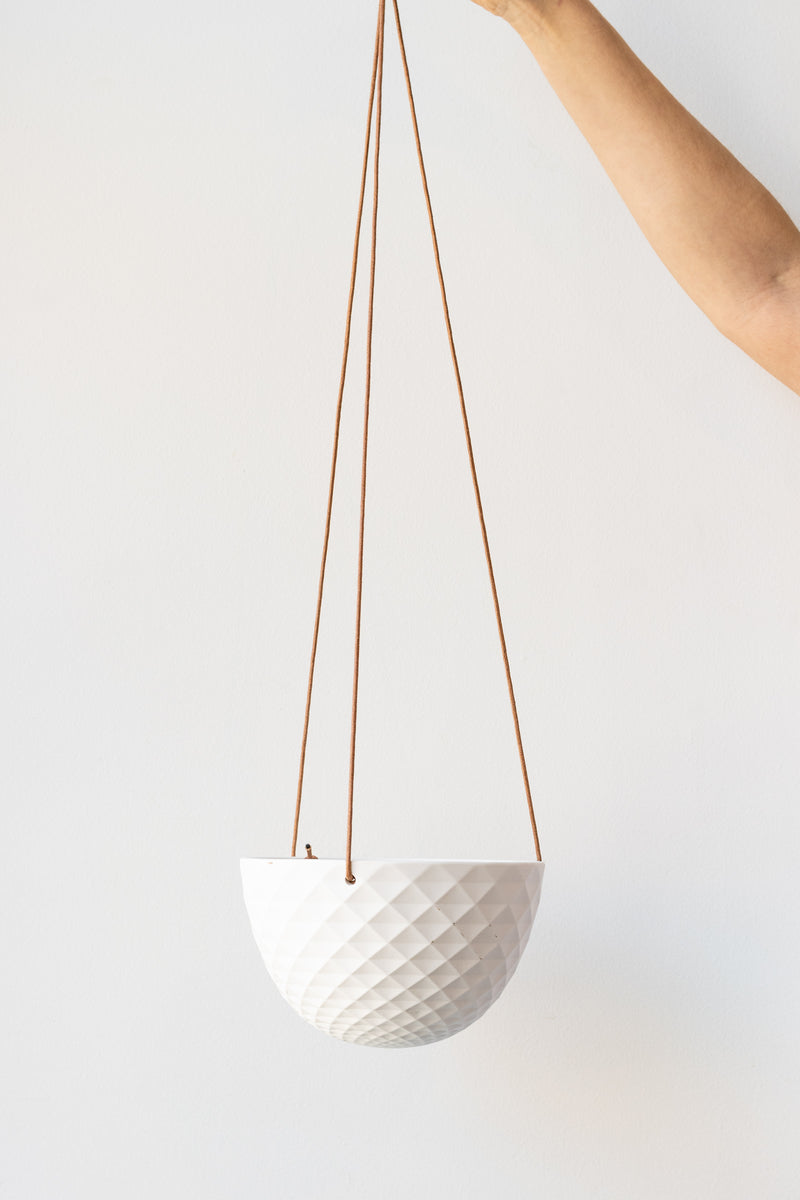 Small round white hanging dish planter held in front of white background