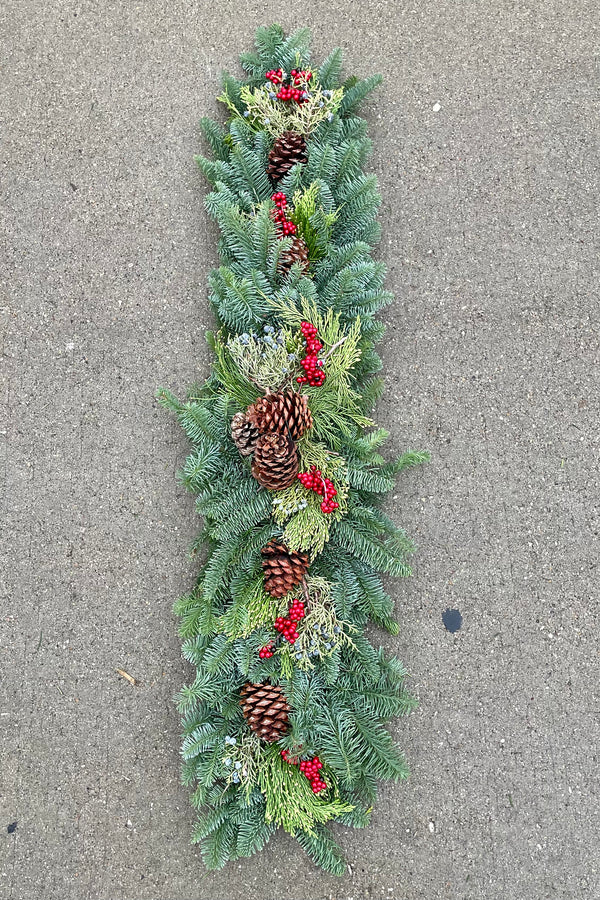 Mantle / Shelf swag piece made from evergreen branch, faux canella berry and pine cones sitting on concrete.