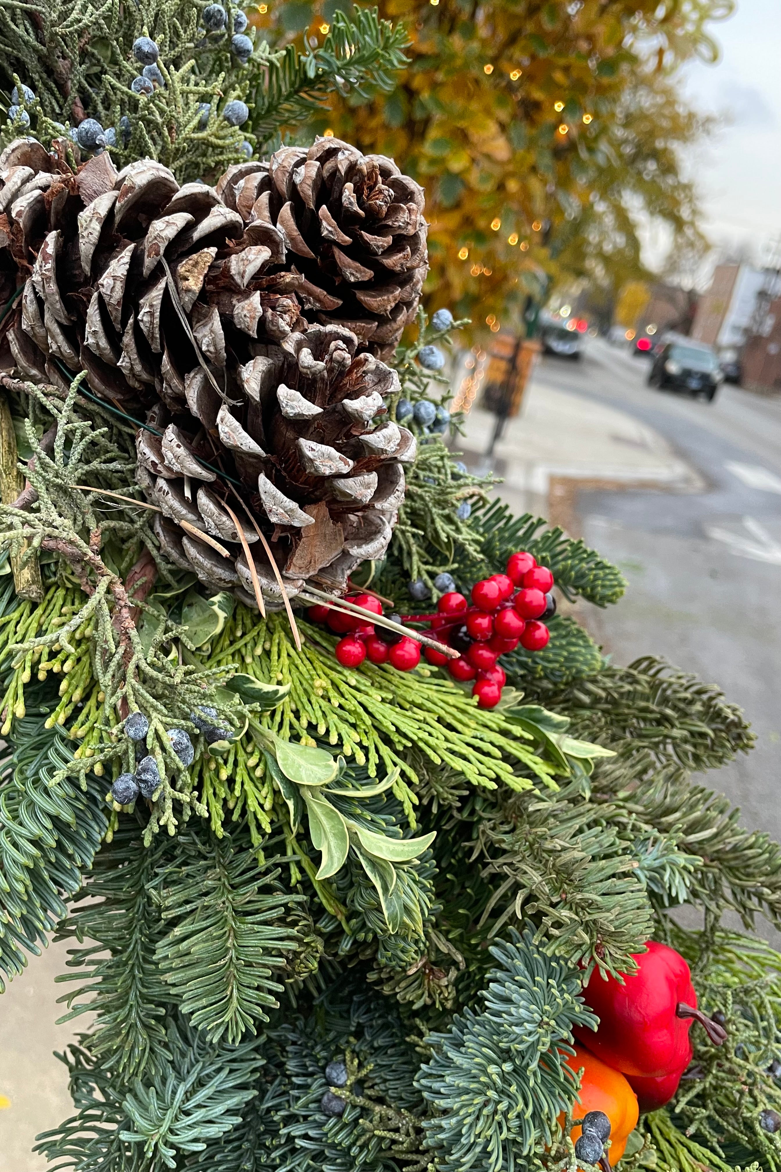 Detail shot of an area of a evergreen swag comprised of evergreen, pinion and faux fruit. 