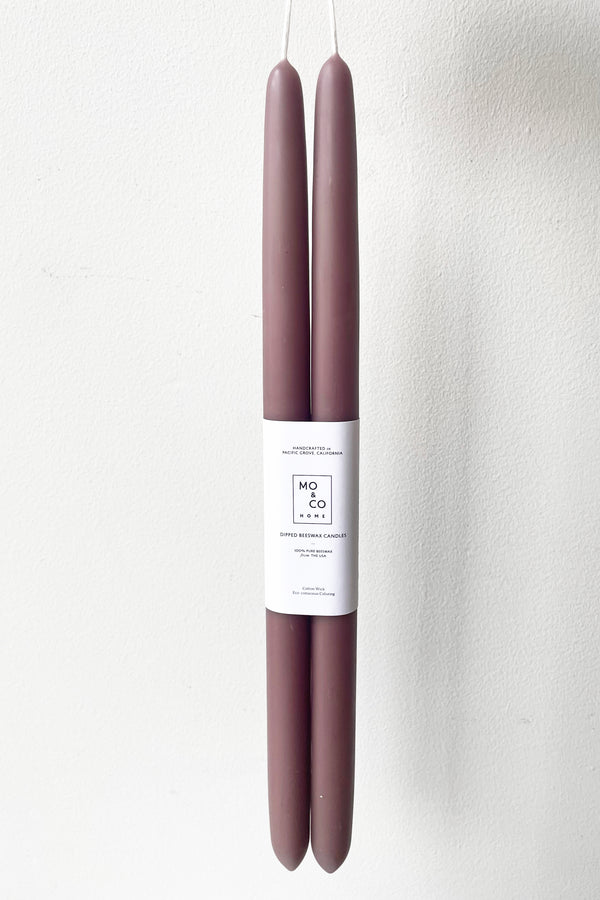 A hand holds the Mauve 14" Taper Candles, pair against a white backdrop