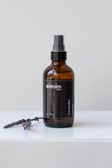 Lavender body mist by EINNIM with two sprigs of lavender on a white surface in front of white background