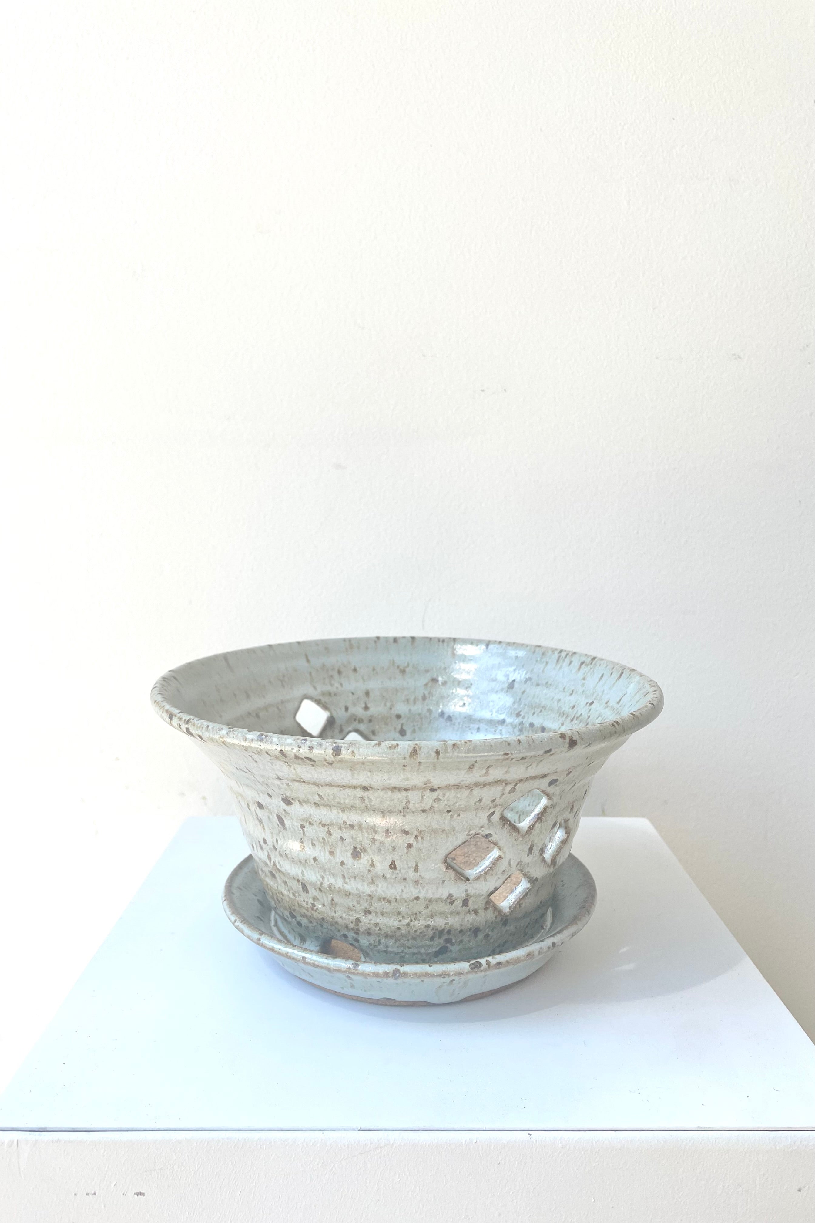 A slight overhead view of the 5" cornflower orchid pot and attached saucer with a view of 4 of the diamond-shaped side drainage holes