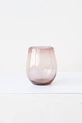 Small garnet oval colored wine glass on a white table in a white room