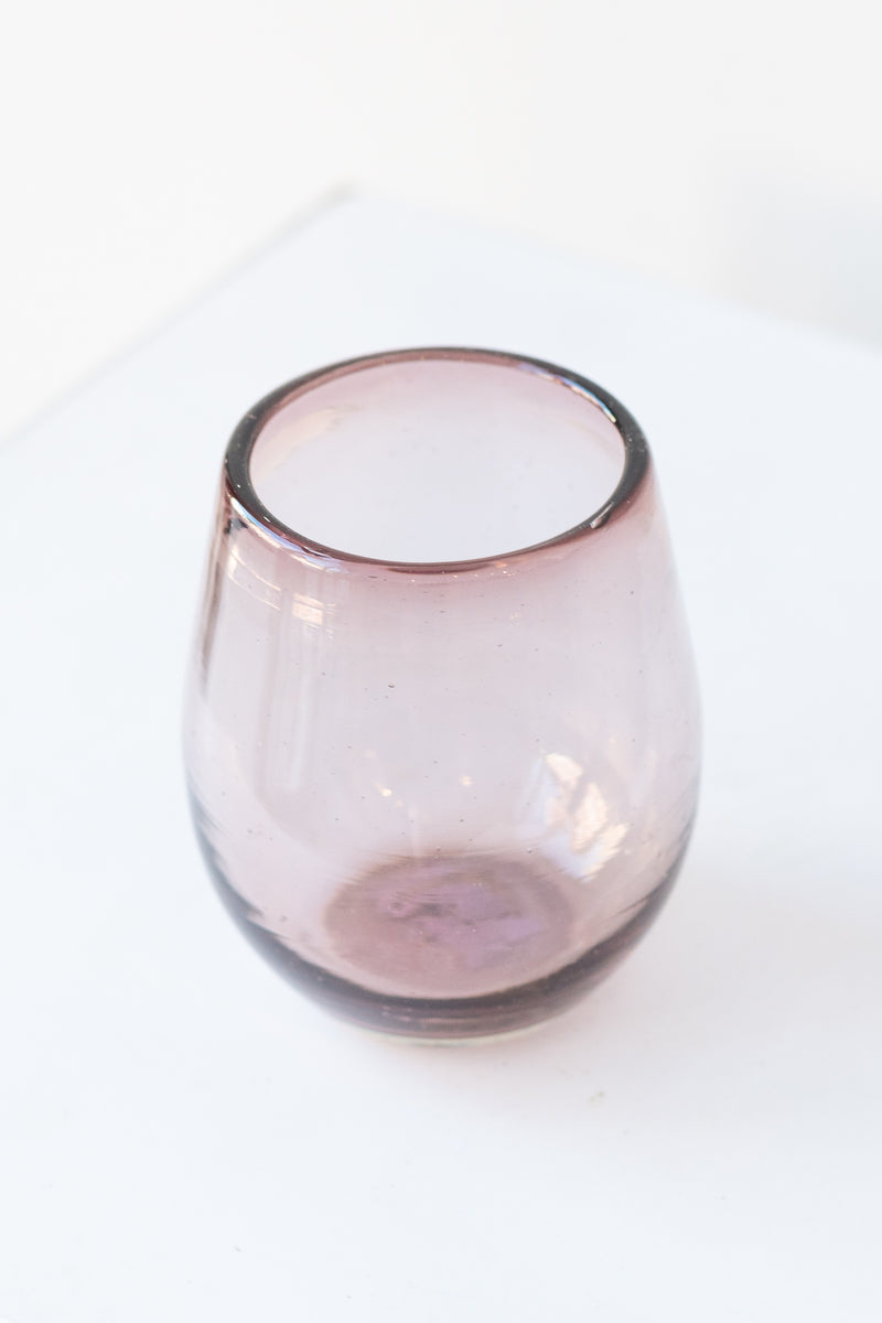 Small garnet oval colored wine glass on a white table in a white room