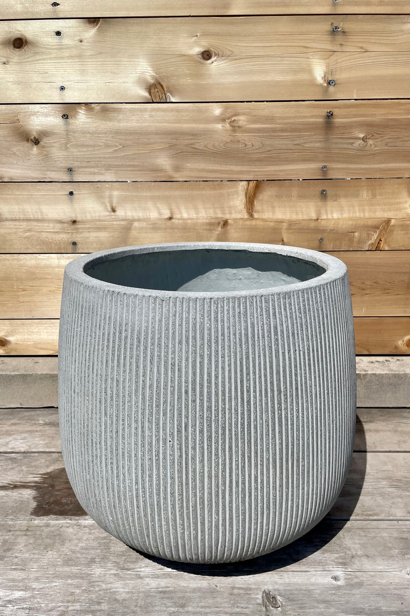 Detail of Pax Pot Vertical Ridged Light Grey Large against a wooden fence