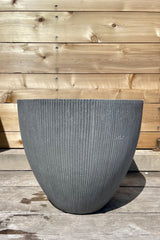 Jesslyn Pot vertical ridged dark grey small against a wooden fence