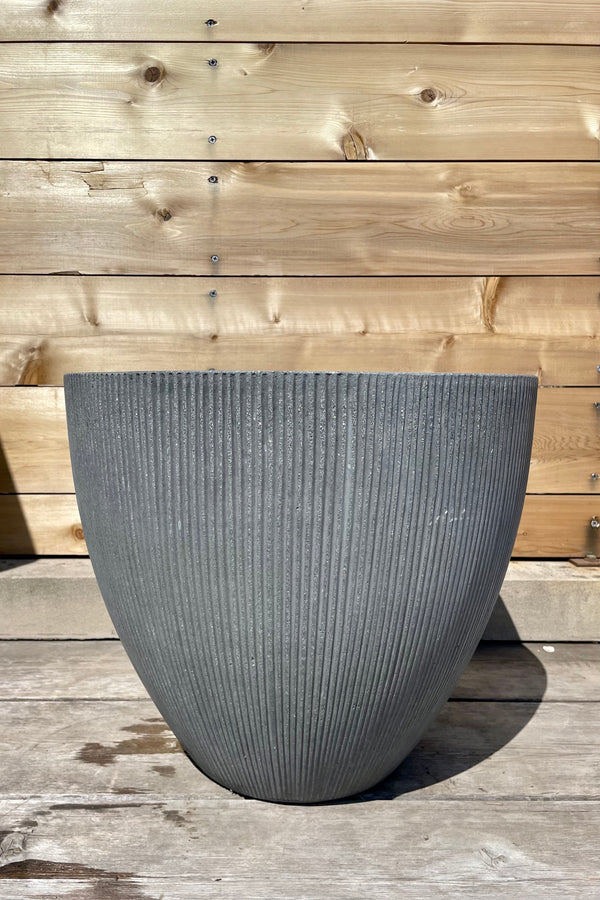 Jesslyn Pot vertical ridged dark grey small against a wooden fence