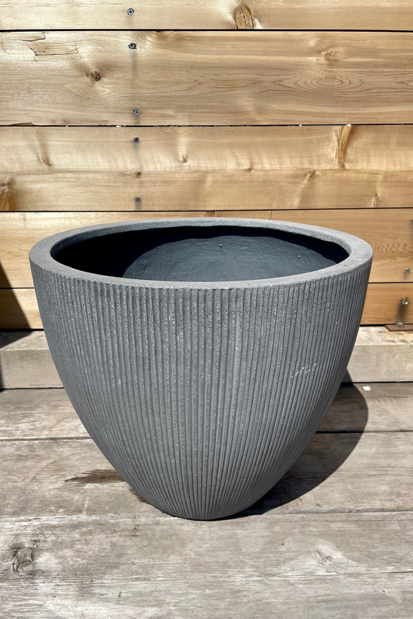 Detail of Jesslyn Pot vertical ridged dark grey small against a wooden fence
