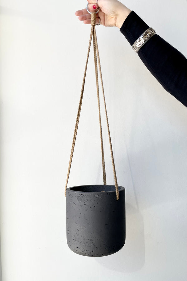 The black washed Charlie hanging pot being help up against a white wall at Sprout Home. 