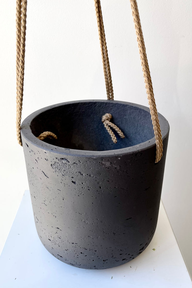 The black washed Charlie hanging pot being help up against a white wall at Sprout Home. 