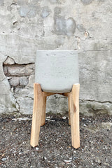 The grey washed extra large part pot with high stand against a concrete wall. 