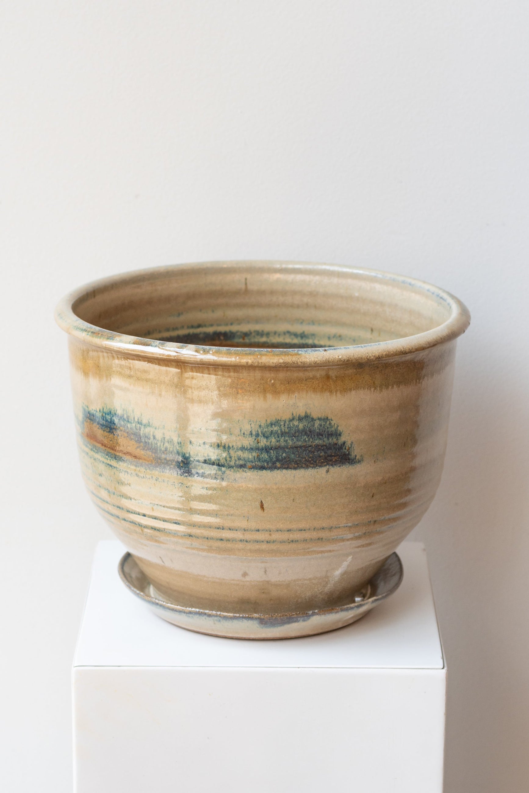 A beige and brown ceramic planter with iron glaze, displayed on a white pedestal. ©Sprout Home
