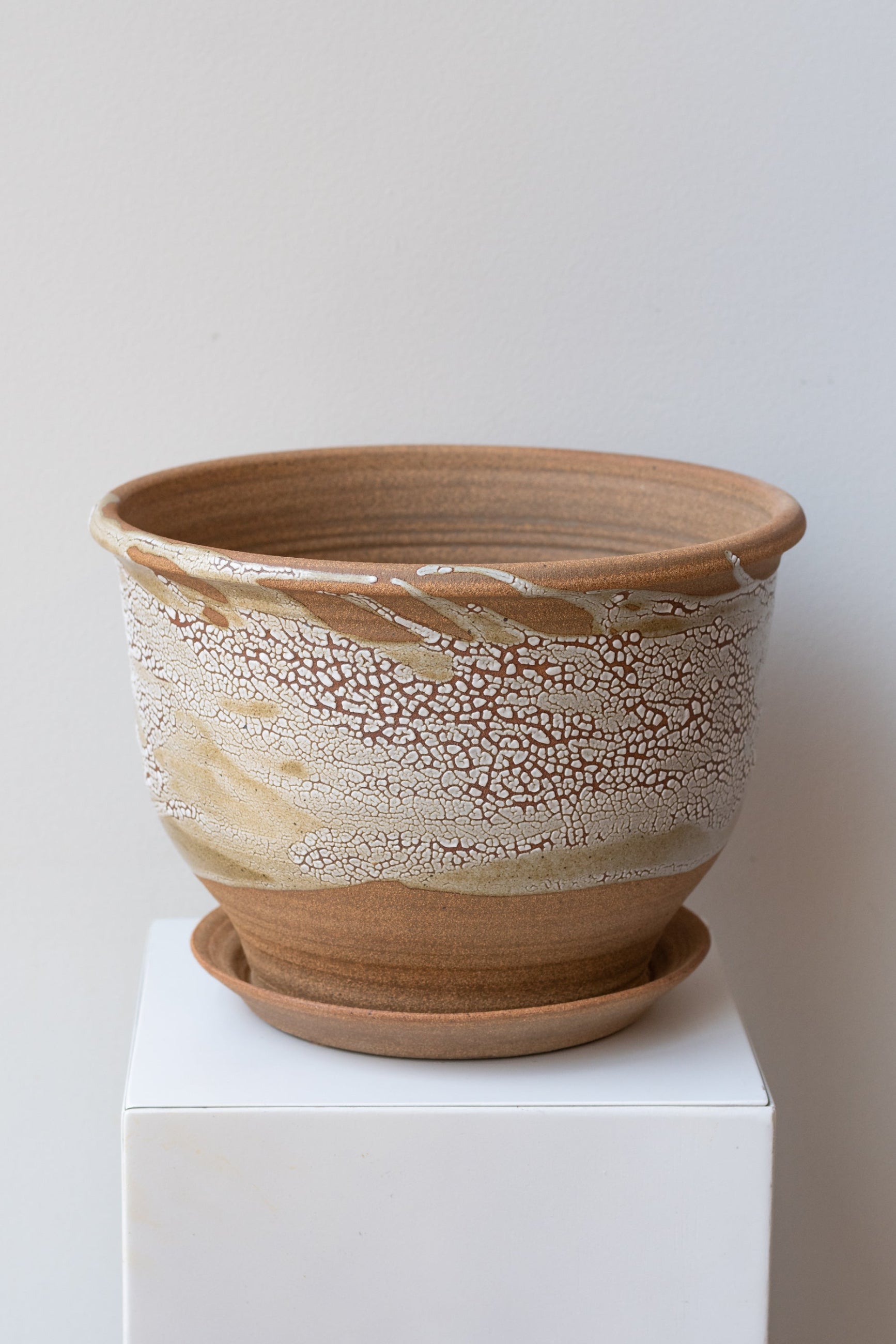 A beige ceramic planter with a crackle glaze pattern, displayed on a white pedestal, with an attached drainage tray. ©Sprout Home