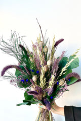 A hand holds Plum Fizz Preserved floral arrangement by Sprout Home against a white backdrop