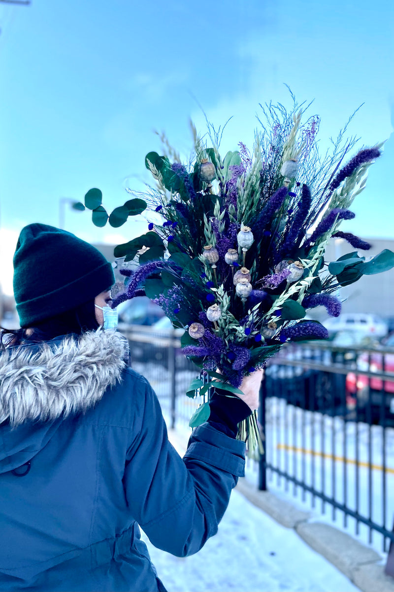 A woman outside lifts up Plum Fizz Preserved floral arrangement by Sprout Home 