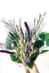 A view of Plum Fizz Preserved floral arrangement by Sprout Home held by a hand against a white backdrop