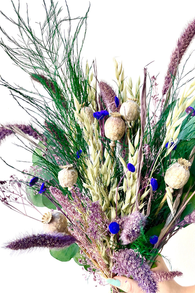 A close-up view of Plum Fizz Preserved floral arrangement by Sprout Home held by hand against a white backdrop
