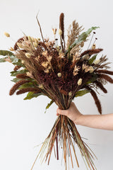Hand holding "Allspice" autumnal floral preserved arrangement by Sprout Home in front of white background