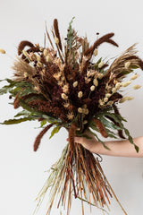 Hand holding large "Allspice" autumnal preserved floral arrangement by Sprout Home in front of white background